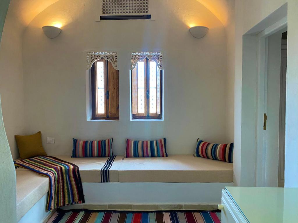 米多恩Hôtel Djerba Authentique - Au centre de Midoun的带枕头的长凳和2扇窗户的客房