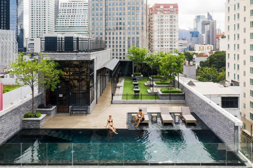 曼谷The Coach Hotel Sukhumvit - Asok BTS Bangkok by Compass Hospitality的两个人坐在一座建筑的顶部的游泳池里