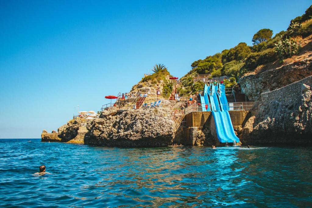 泰拉西尼CDSHotels Terrasini - Città del Mare的悬崖边的水中一组蓝色的伞