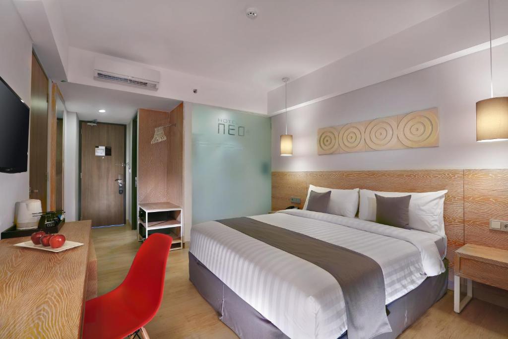 勒吉安Hotel NEO+ Kuta Legian by ASTON的酒店客房设有一张大床和一张红色椅子。