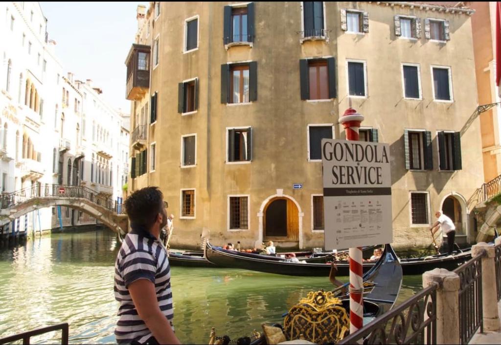 威尼斯Anzolo Palace - Rooms & Apartments的一个小男孩,站在运河上的桥上,坐船