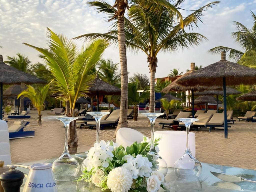 萨利波图尔Movenpick Resort Lamantin Saly的沙滩上一张桌子,上面放着酒杯和鲜花