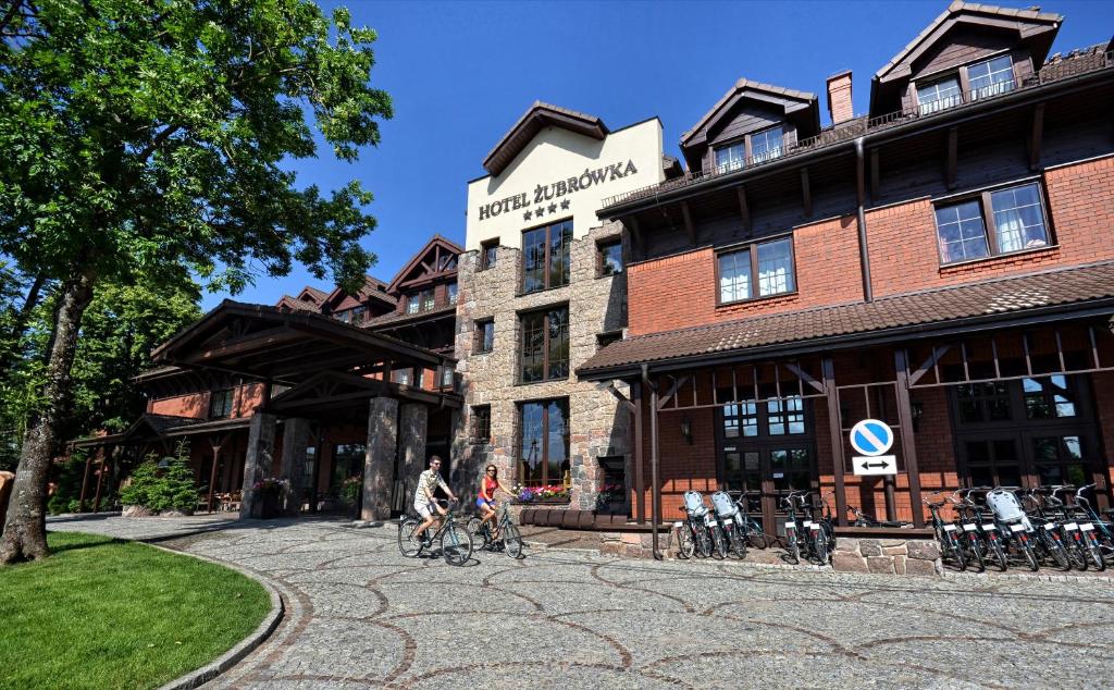 比亚沃维耶扎Hotel Żubrówka Spa & Wellness的两人骑车在大楼前