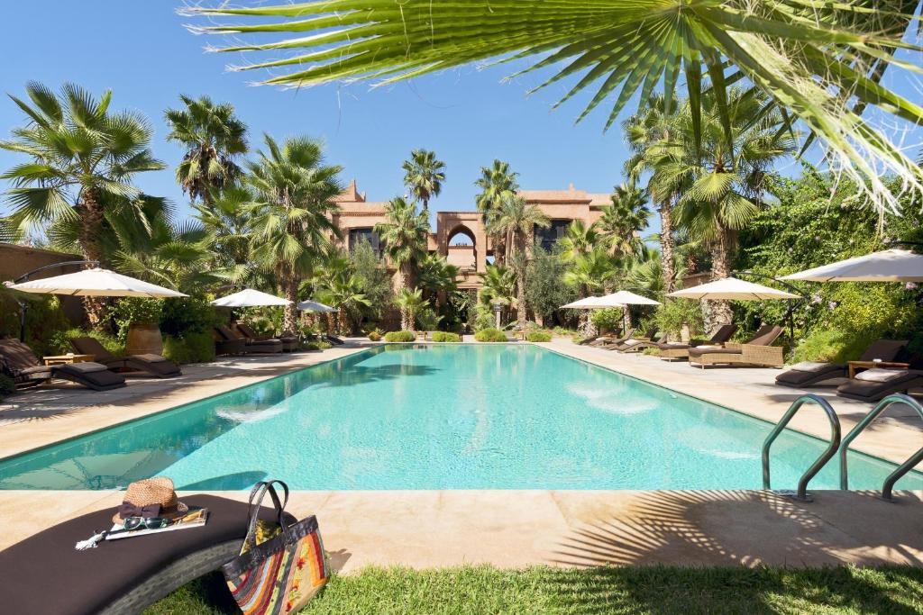 马拉喀什Tigmiza Boutique Hotel & Spa的棕榈树和遮阳伞度假村的游泳池