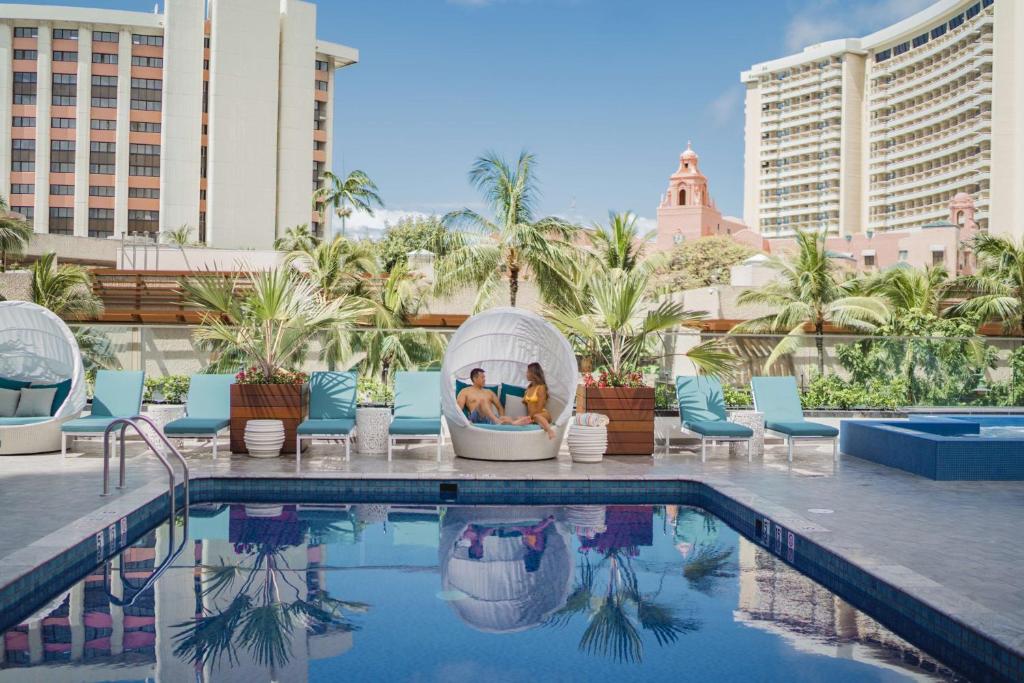 檀香山OUTRIGGER Waikiki Beachcomber Hotel的一座酒店游泳池,有两人坐在iguana