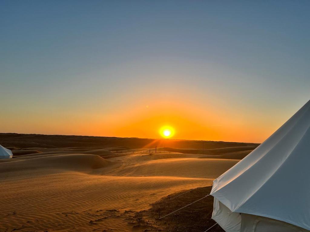 ShāhiqDesert Private Camps -ShootingStar Camp的沙漠中的日落,前方有帐篷