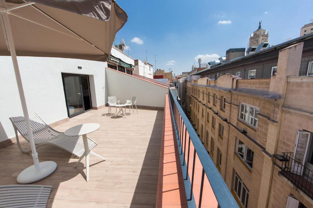 马德里Apartamentos Centro Jardines的大楼内的阳台配有椅子和遮阳伞