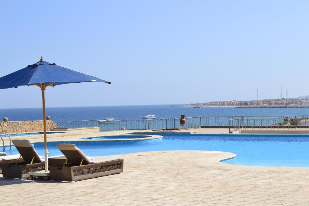 艾因苏赫纳La Siesta Hotel Al Sokhna的一个带椅子和遮阳伞的游泳池以及大海