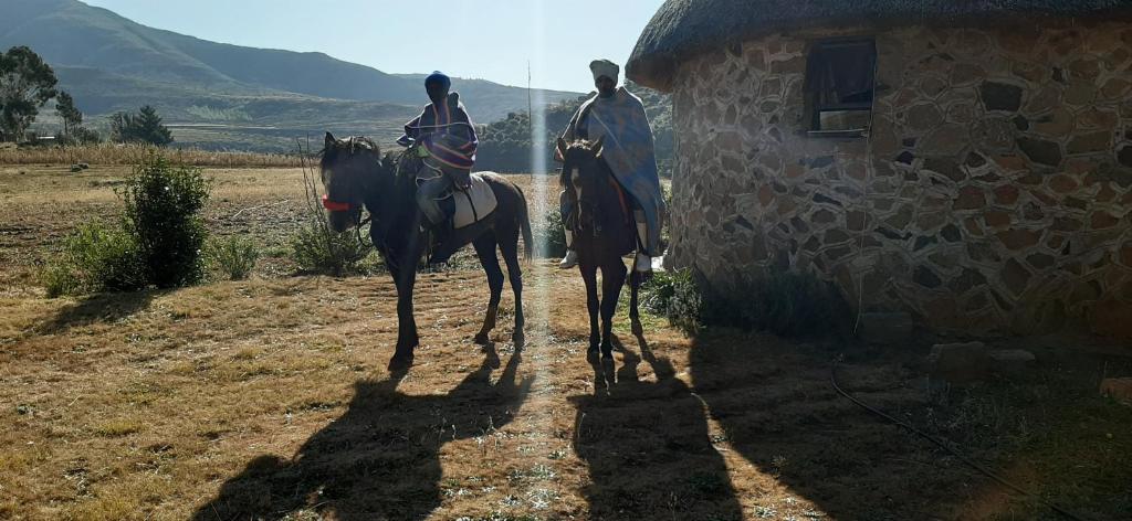 Casa Tumi Round Houses.的两个人在建筑物旁边的土路上骑马