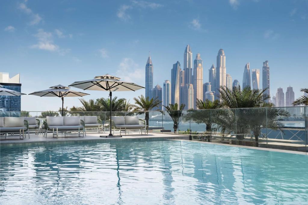 迪拜Radisson Beach Resort Palm Jumeirah的一个带椅子和遮阳伞的游泳池,并享有城市天际线