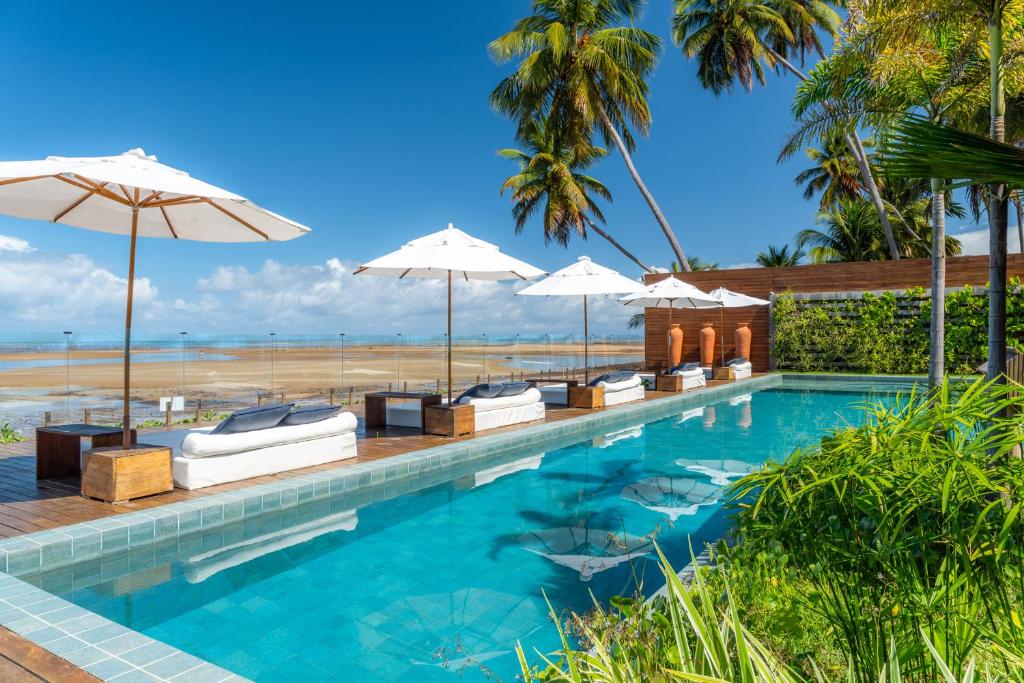 马拉戈日Villa Pantai Boutique Hotel Maragogi的一个带遮阳伞的游泳池和一个海滩