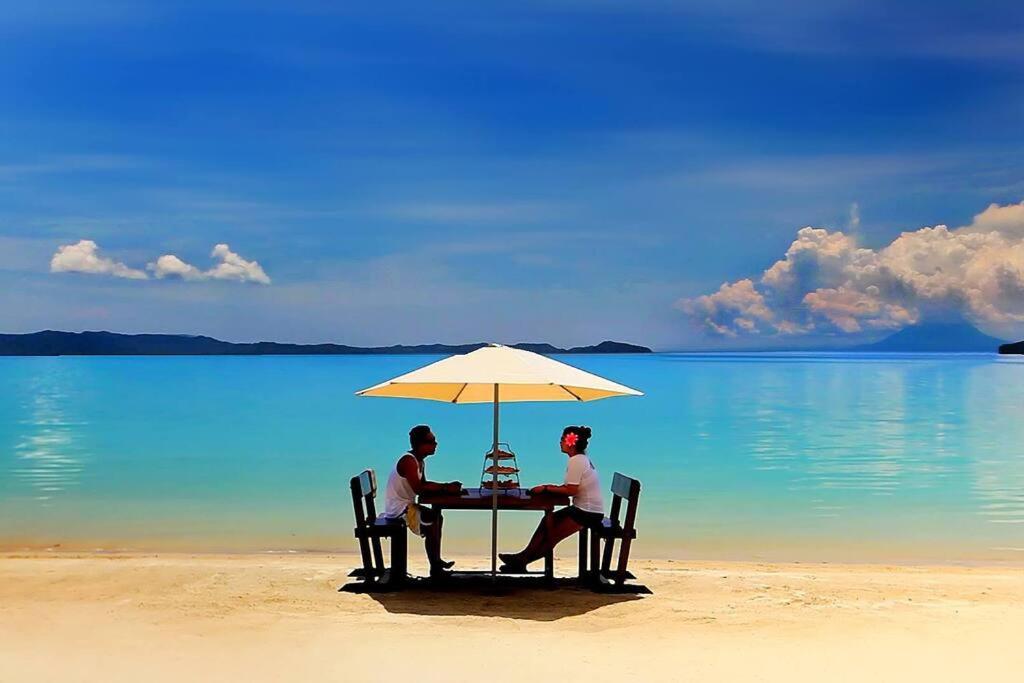 圣维森特Gilligans Port Barton Beach Resort的坐在海滩上一把伞下的桌子上的一对夫妇