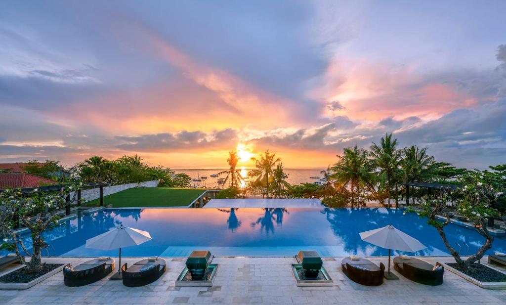 沙努尔InterContinental Bali Sanur Resort, an IHG Hotel的日落前带椅子和遮阳伞的游泳池