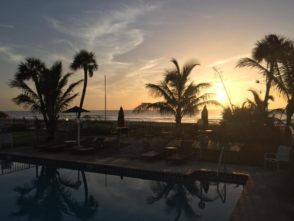 可可比奇冲浪工作室海滩度假公寓式酒店的日落时分棕榈树和海洋的游泳池