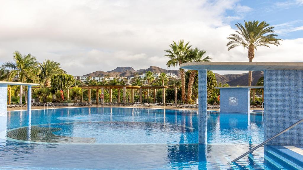 普雷塔斯Playitas Aparthotel - Sports Resort的棕榈树和山脉度假村的游泳池