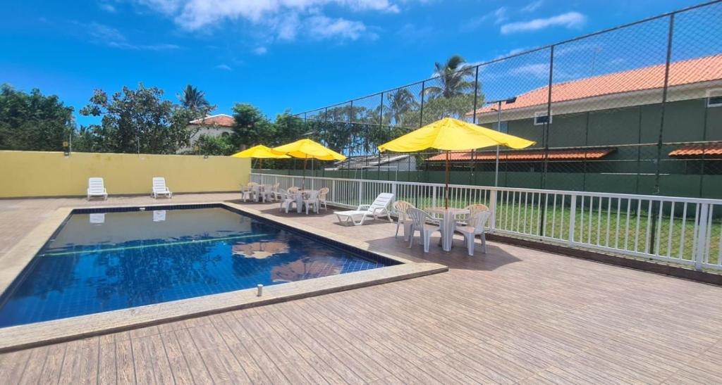 卡马萨里Village de Praia Duplex Arembepe的一座带椅子和遮阳伞的游泳池位于一座建筑旁边