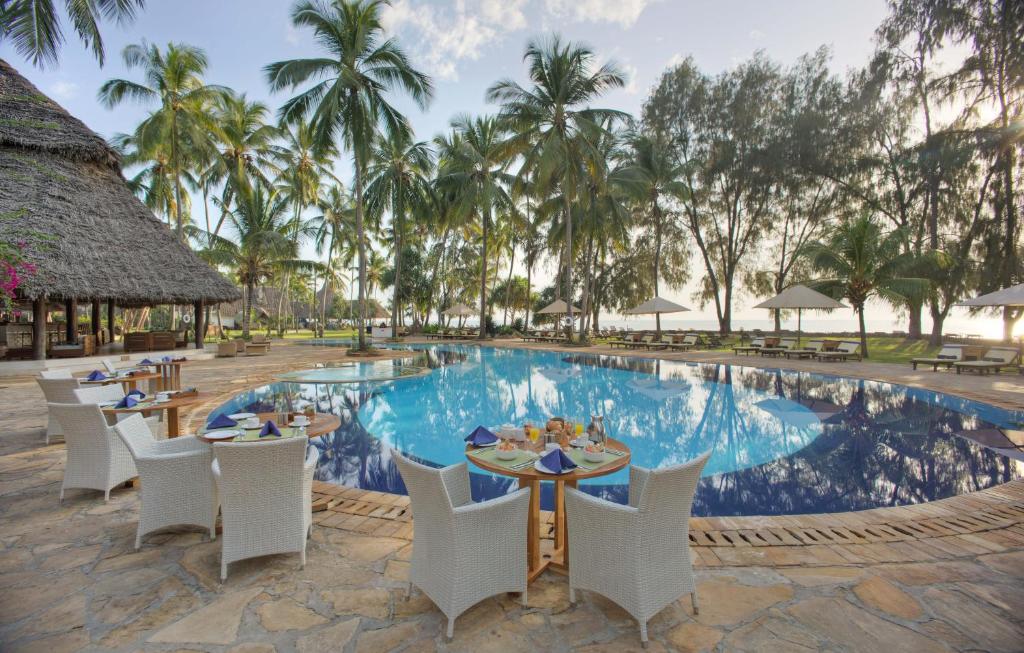 吉汶瓦蓝色海湾度假酒店及水疗中心的一个带桌椅的度假村游泳池,并种植了棕榈树