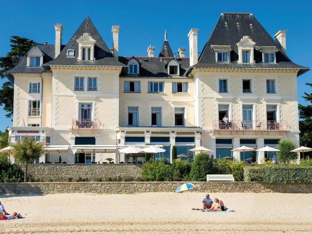 拉波勒卡罗琳别墅蓝色假日酒店的坐在海滩上,在大房子前面的人