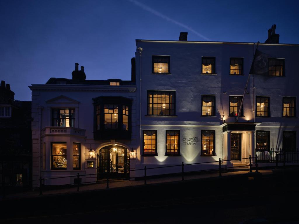 利明顿Stanwell House的一座白色的大建筑,晚上有明亮的窗户