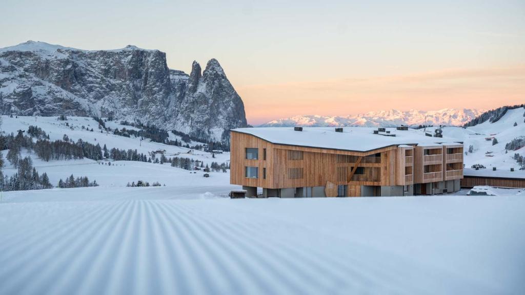 阿尔卑斯休斯山ICARO Hotel的一座雪地中的建筑,背景是一座山