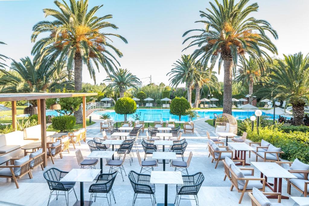 罗希姆诺五月海滩酒店的一间设有桌椅的餐厅,种植了棕榈树