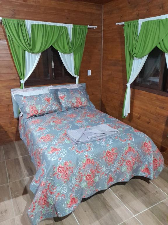 圣弗朗西斯科-迪保拉Cabanas dos Pinheiros的一张带蓝色棉被和绿色窗帘的床