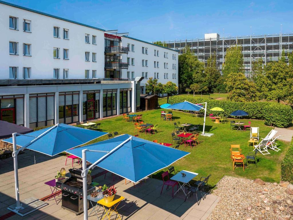 达姆施塔特Greet hotel Darmstadt - an Accor hotel -的户外庭院配有桌椅和蓝色遮阳伞。