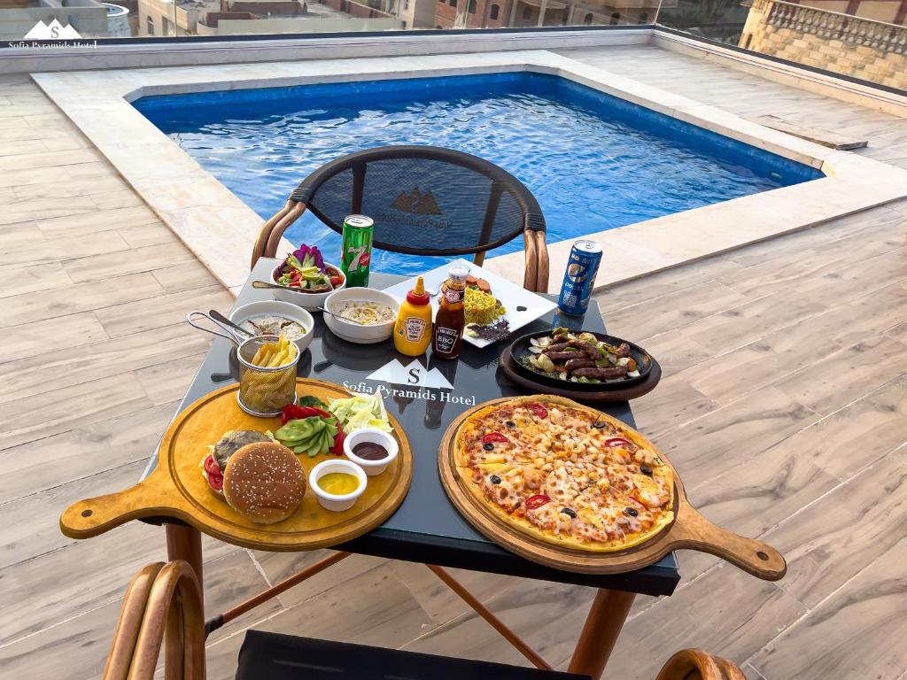 开罗Sofia Pyramids Hotel的游泳池旁的餐桌上摆着比萨饼和食物