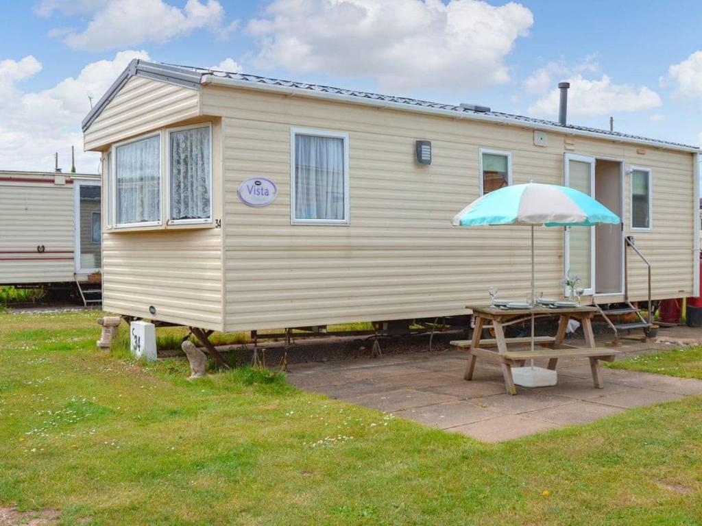 伯克顿Norfolk Lavender Caravan - Sleeps 4 - WiFi and Sky TV Included的一个带野餐桌和雨伞的房子