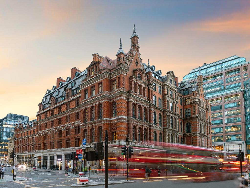 伦敦伦敦利物浦街安达仕 - 凯悦构想酒店的一辆红色的公共汽车驶过一座大型砖砌建筑