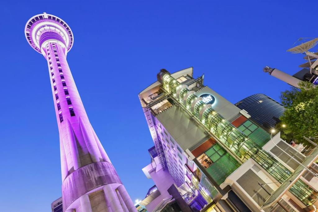奥克兰CBD Stunner - Skytower View - WIFI - Netflix的一座高大的紫色塔楼,位于一些建筑前面