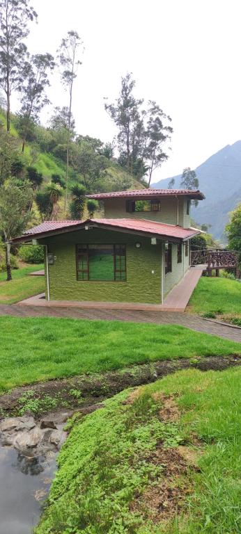巴尼奥斯"Casa Verde" en Baños de Agua Santa con vista al volcán Tungurahua的一座绿色建筑,位于一座带草地的山丘上