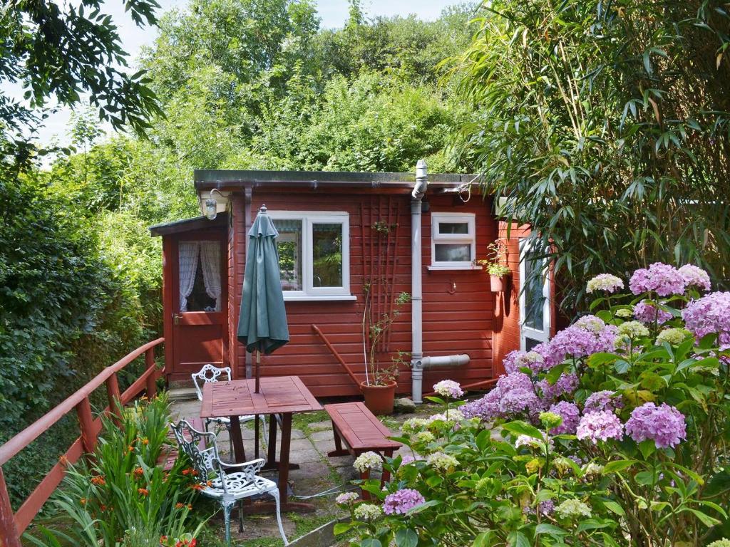 Crackington Haven切特里瓦撒乡村别墅的一座红色的小房子,配有野餐桌和一些鲜花