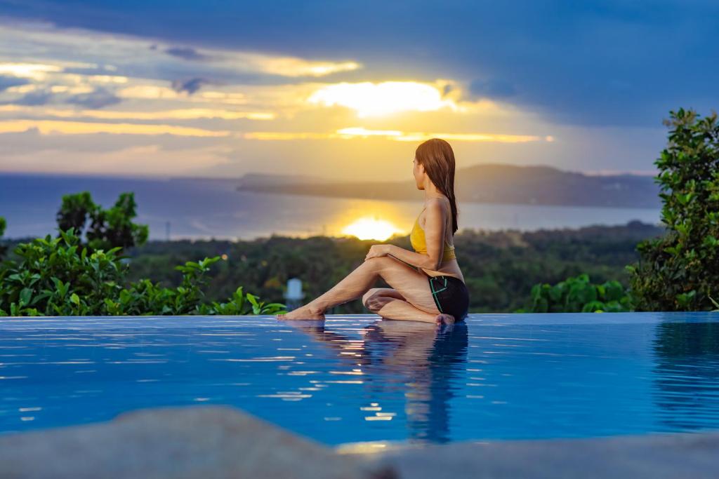 Baclayon马克西斯日出日落Spa度假村的坐在游泳池边欣赏日落的女人