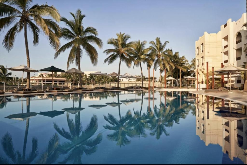 塞拉莱Hawana salalah Apartment的棕榈树和建筑度假村的游泳池