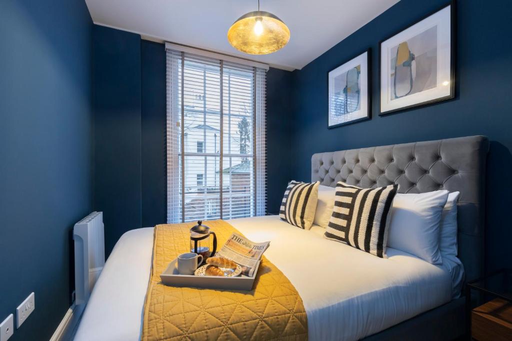 切尔滕纳姆Elliot Oliver - Luxury 2 Bedroom Regency Apartment With Parking & EV Charger的蓝色的卧室,配有一张床和食物托盘