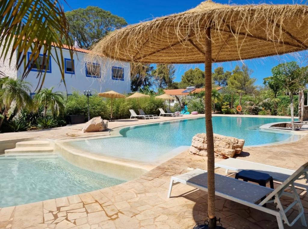 阿尔戈什Superbe villa avec piscine en algarve的一个带草伞和椅子的度假游泳池