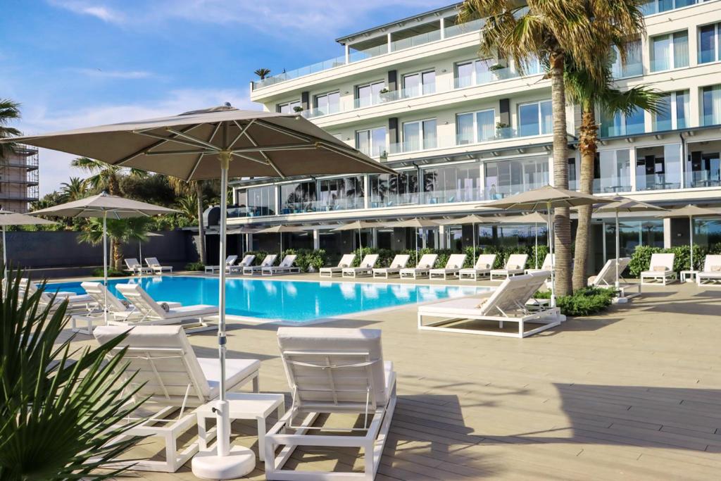 波蒂奇Hotel & Resort Tre Fontane Luxury的一个带椅子和遮阳伞的游泳池以及酒店