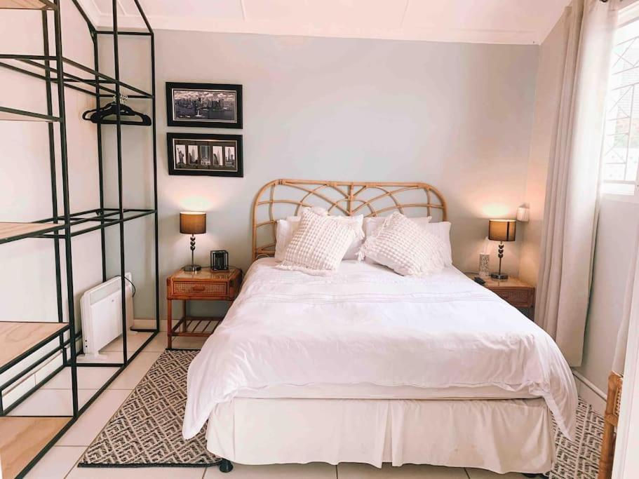 德班Stunning 1 bed cottage in Durban North的卧室配有一张白色床、两张桌子和两盏灯。