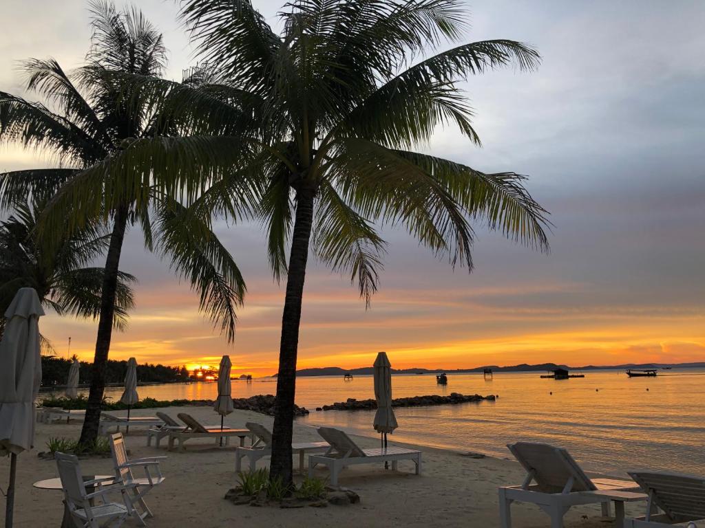 富国Gold Coast Phu Quoc Beach Resort的日落时分带椅子和棕榈树的海滩
