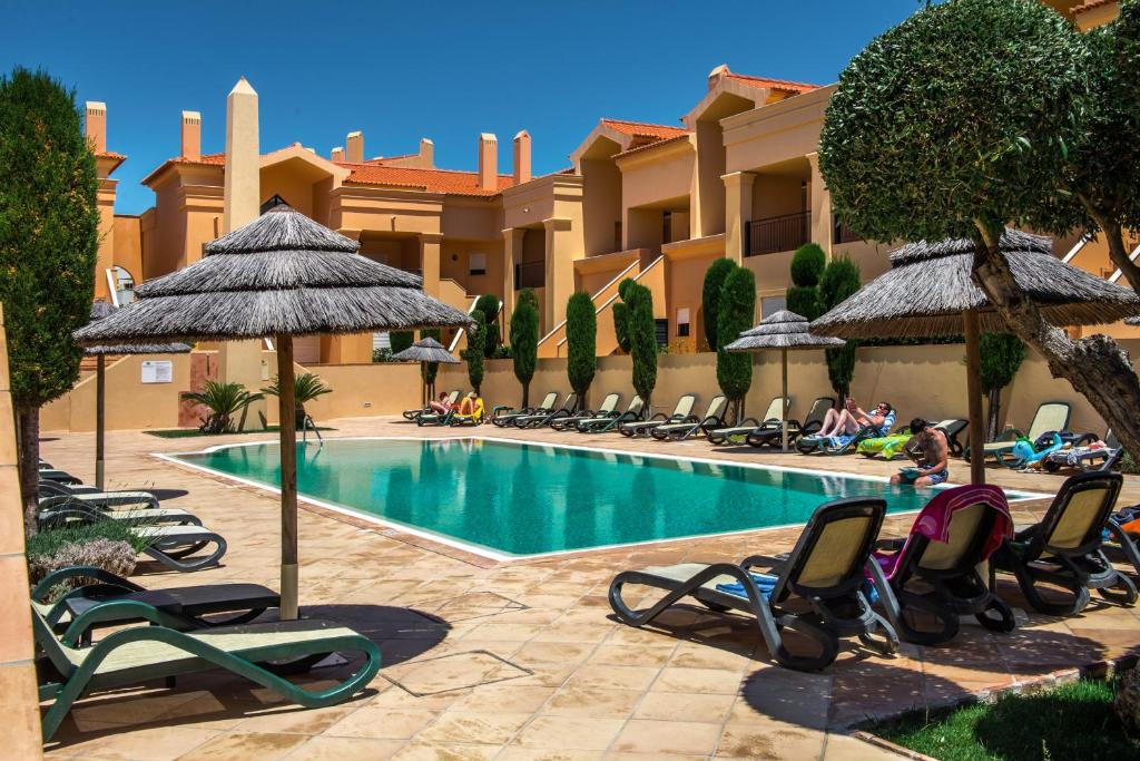 卢斯Baia da Luz Resort的一个带草坪椅和遮阳伞的游泳池的度假酒店
