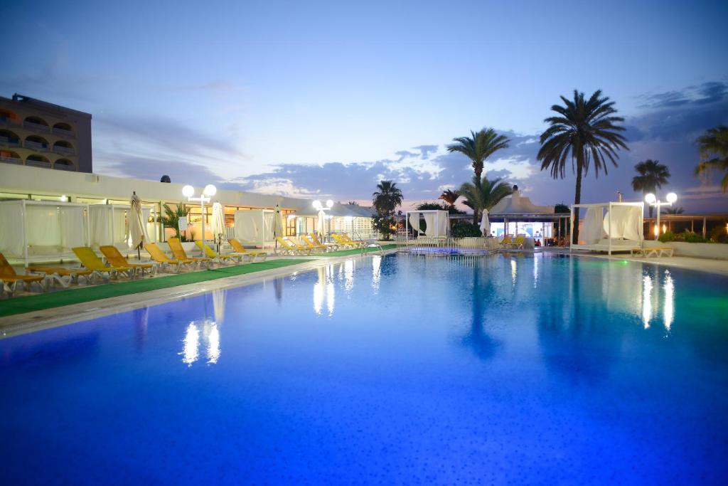 莫纳斯提尔One Resort Jockey Monastir的一个带椅子和棕榈树的大型蓝色游泳池
