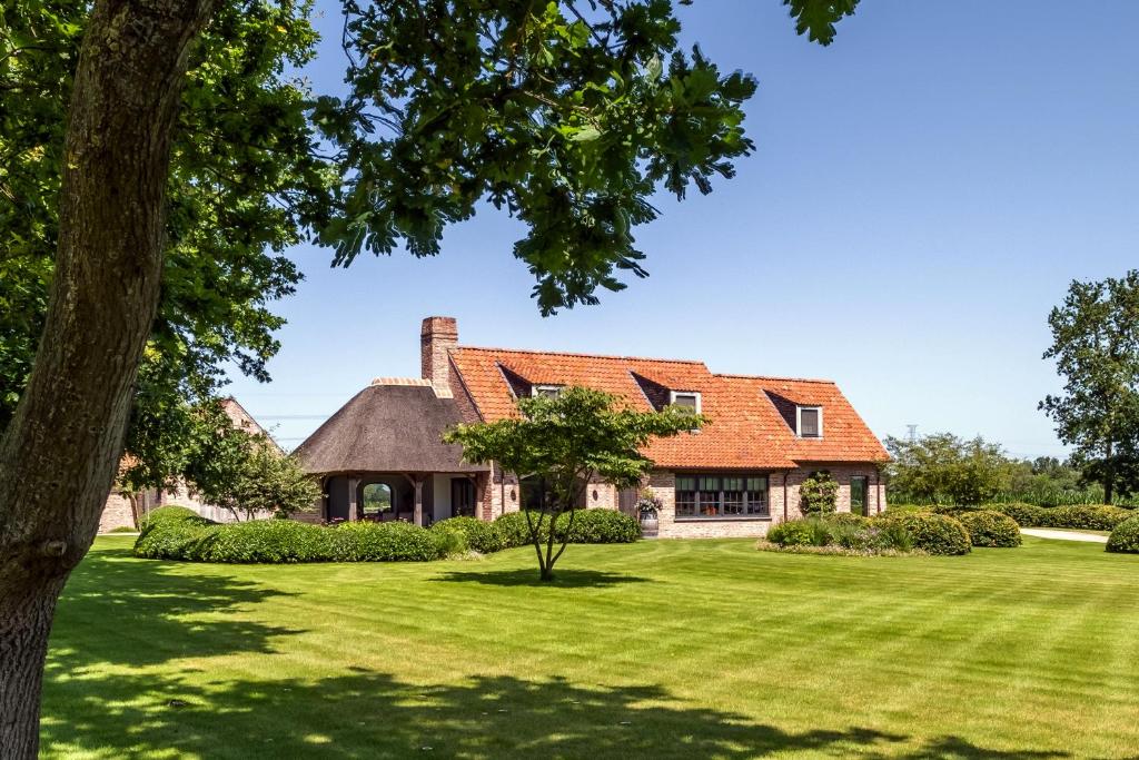 达默Hoeve den Akker - luxueuze vakantiewoningen met privétuinen en alpaca's nabij Brugge, Damme, Knokke, Sluis en Cadzand的一座带橙色屋顶和绿色庭院的房子