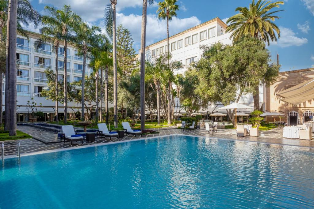 拉巴特拉图尔哈桑宫酒店的一座带椅子和棕榈树的游泳池,位于一座建筑前