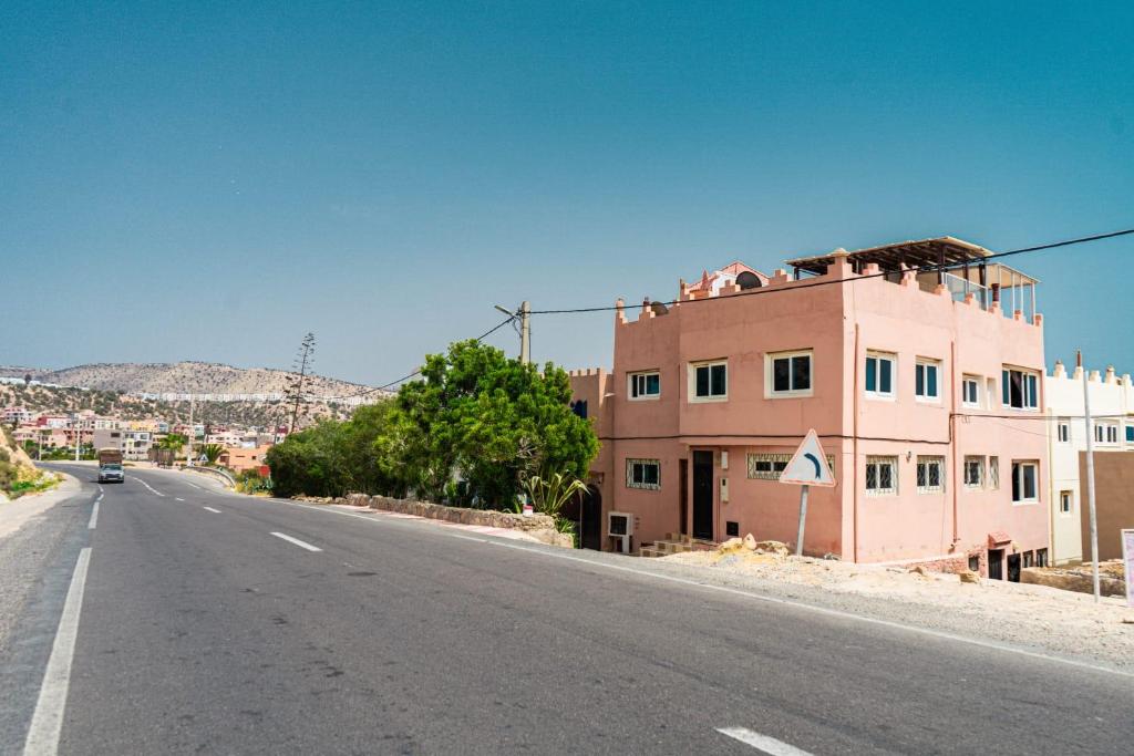 阿加迪尔Appartement en bord de Mer Dar imi的一条空的路,边有一座粉红色的建筑