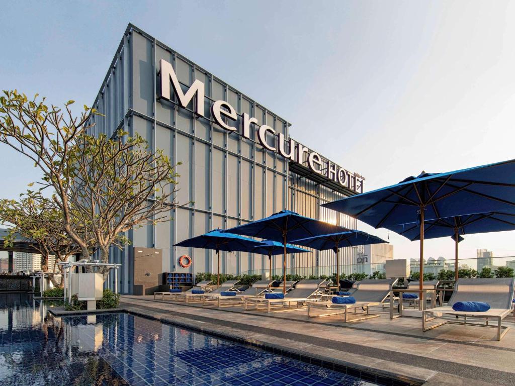 曼谷曼谷素坤逸 24 号美居酒店的游泳池旁的酒店拥有椅子和遮阳伞