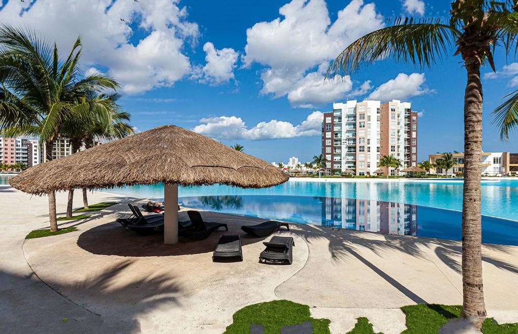 坎昆Departamento 'Hozanek' en Dream Lagoons Cancun的一个带草伞和椅子的海滩和一个游泳池