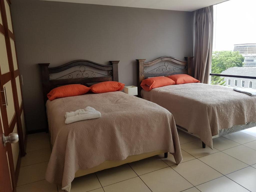 危地马拉Apartamento Reforma Ciudad de Guatemala的一间卧室配有两张带橙色枕头的床和窗户。