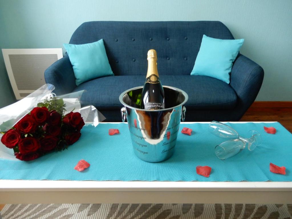 梅尔·莱斯·拜恩斯Villa des Bains de Mer avec balcon et vue, terrasse 300 m plage, 2 chambres, 3 velos fournis à Mers les Bains Le Treport, petit dejeuner en option的一瓶香槟,放在一张带玫瑰的桌子上的桶里