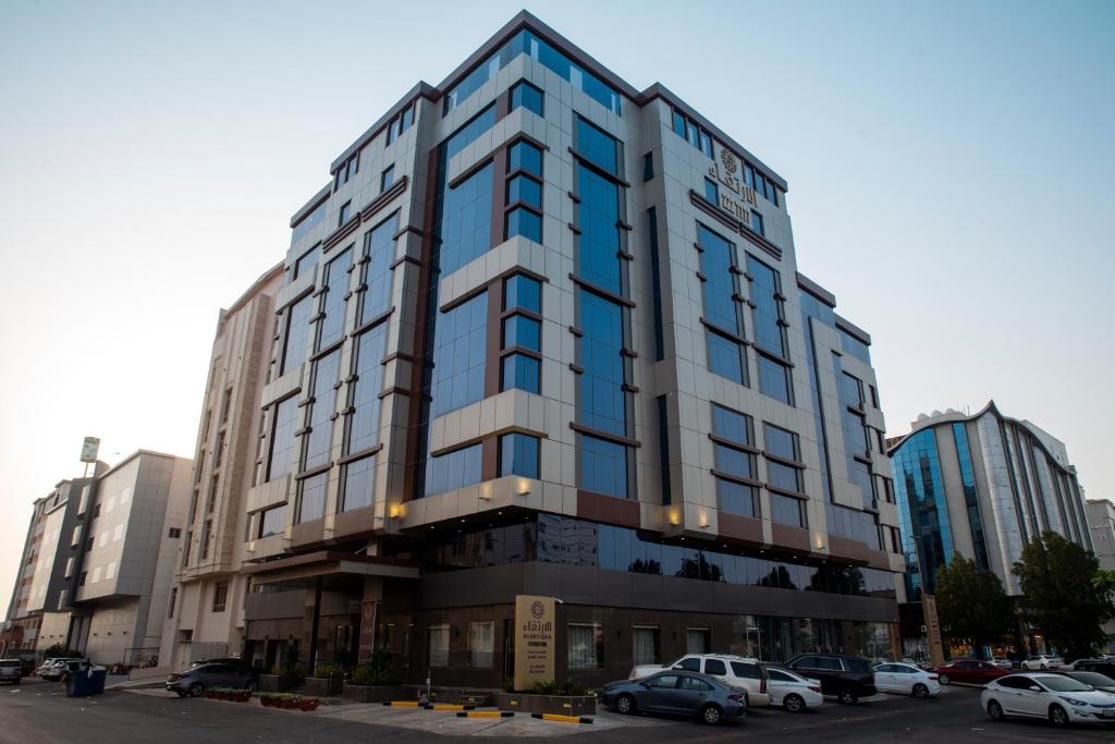 吉达Al Ertiqaa Hotel的停车场内有车辆停放的高楼